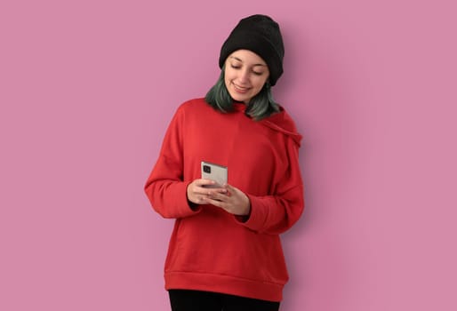 Cute young girl with blue hair using mobile phone, typing a message over pink background