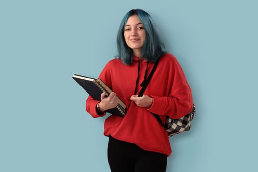 Cute young gilr student with blue hair books and a backpack over a cyan background