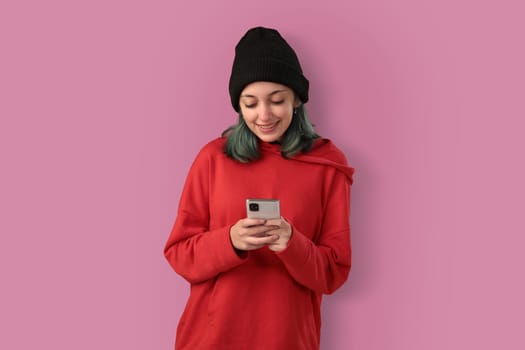 Cute young girl with blue hair using mobile phone, typing a message over pink background