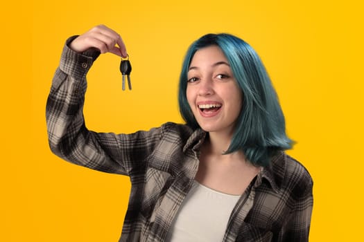 Smiling young woman student with blue hair holding keys over yellow background