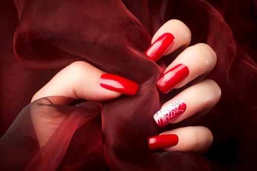 Female hand with beautiful red nails on red background, nail care and manicure concept.