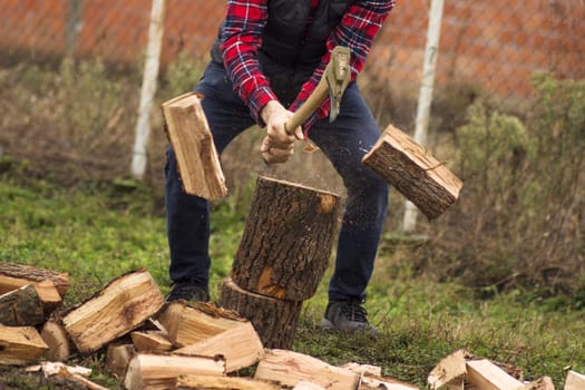 The lumberjack or woodcutter is cutting wood or firewood with axe outdoors.