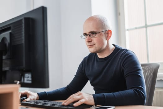 Young Entrepreneur Wearing Eyeglasses Sitting at his Table Inside the Office, Looking at the Report on his Computer Screen