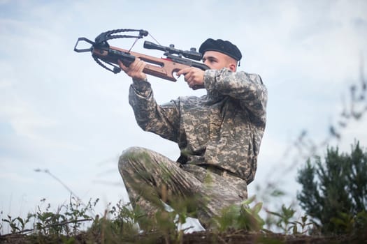 The army soldier in military uniform is aiming with crossbow weapon outdoors.