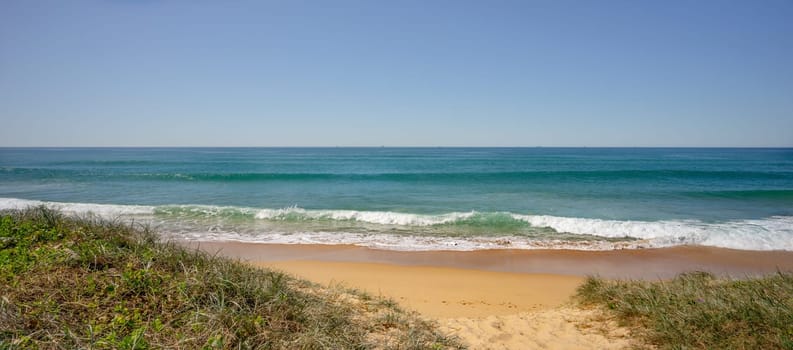 The Buddina foreshore with grassy vegetation on sand dunes and surf waves breaking on the sea shore. A peaceful scene on a calm, winter day in South East Queensland.