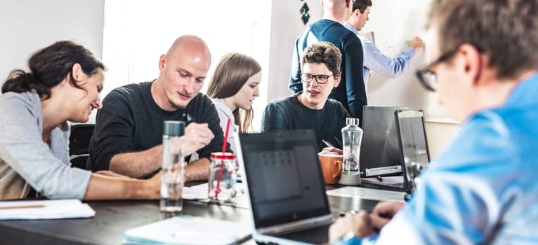 Startup business and entrepreneurship problem solving. Young AI programmers and IT software developers team brainstorming and programming on desktop computer in startup company share office space