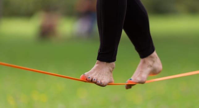Lady practising slack line in the city park. Slacklining is a practice in balance that typically uses nylon or polyester webbing tensioned between two anchor points.