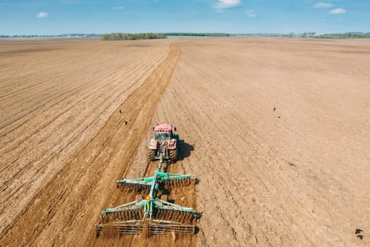 Aerial View. Tractor Plowing Field In Spring Season. Beginning Of Agricultural Spring Season. Cultivator Pulled By A Tractor In Countryside Rural Field Landscape.