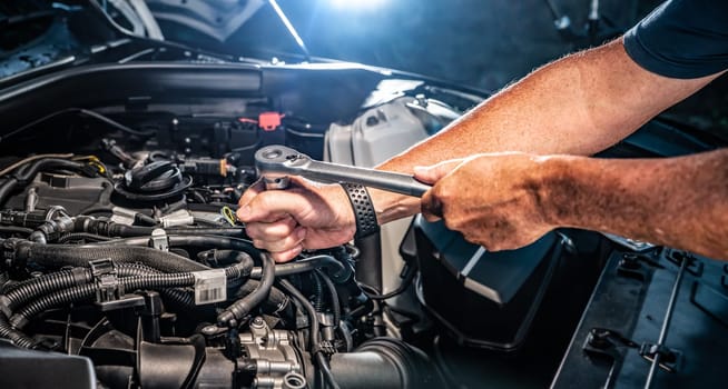 Auto mechanic working on car engine in mechanics garage. Repair service. authentic close-up shot - selective focus with motion blur