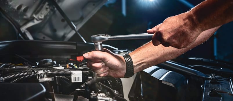 Auto mechanic working on car engine in mechanics garage. Repair service. authentic close-up shot - selective focus with motion blur