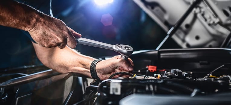 Auto mechanic working on car engine in mechanics garage. Repair service. authentic close-up shot - selective focus with motion blur