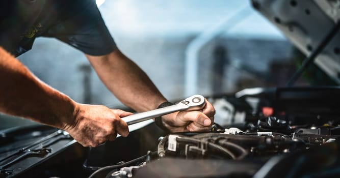 Auto mechanic working on car engine in mechanics garage. Repair service. authentic close-up shot - selective focus with motion blur