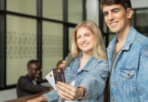 Smiling couple travelers in blue jeans paying with credit card for hotel room or airport lounge. Family travel vacation concept