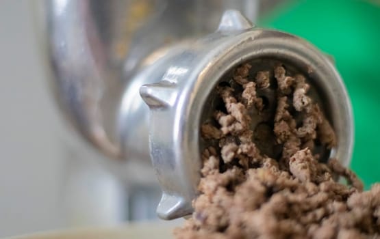 Minced meat in a manual mechanical meat grinder. Fresh boiled meat is ground with an old metal meat grinder, close-up in the kitchen
