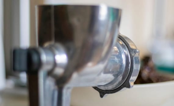 The classic manual iron meat grinder is fixed on the table. Antique, vintage meat grinder in the kitchen, close-up. The meat grinder is ready to go