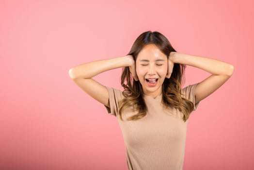 Asian portrait beautiful young woman have close ears with hand palms and close eyes, studio shot isolated on pink background, Thai female covering ears for loud noise with copy space, bad pressure