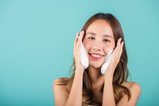 Asian woman face wash exfoliate scrub soap foam with skincare cleansing, Portrait beautiful female smile applies foaming cleanser healthy skin, Studio isolated on blue background, beauty skincare