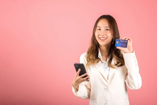 Happy Asian portrait beautiful cute young woman excited smiling hold mobile phone and plastic debit credit bank card, studio shot isolated on pink background, female using smartphone online shopping