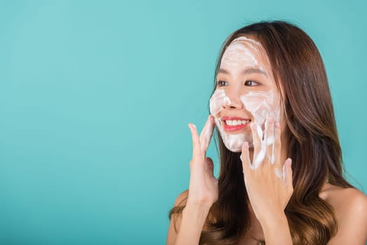 Asian woman face wash exfoliation scrub soap with skincare cleansing, Portrait beautiful female smile applies foaming cleanser healthy skin, Studio isolated on blue background, skincare daily routine