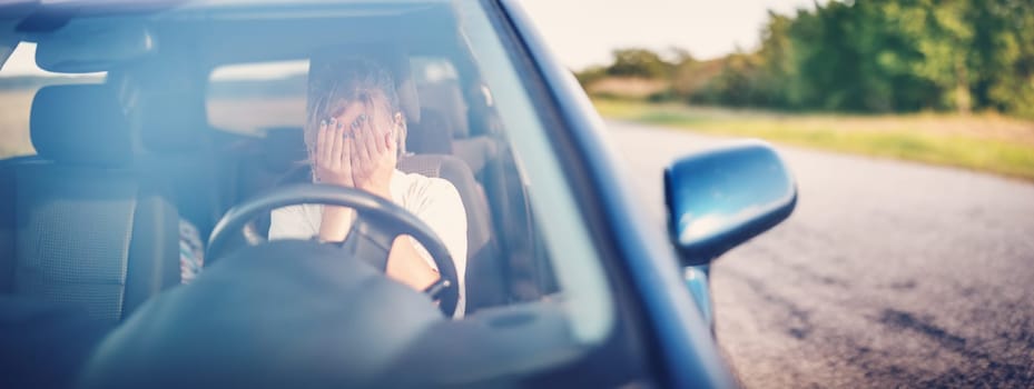 Upset woman sitting in the car and covering face with her hands. Concept of a accident and traffic violations.