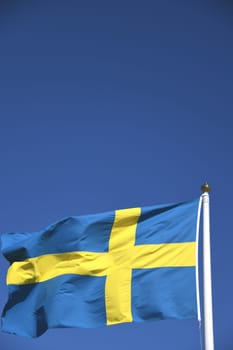 The national flag of Sweden in the colors blue and yellow waves in the wind on a flagpole. The krone is the currency of Sweden. The blue sky serves as the background.