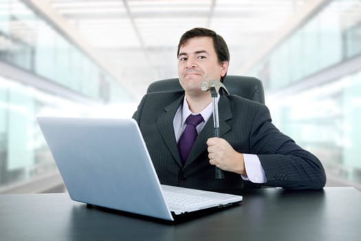 young crazy businessman with a hammer smashing a laptop, at the office
