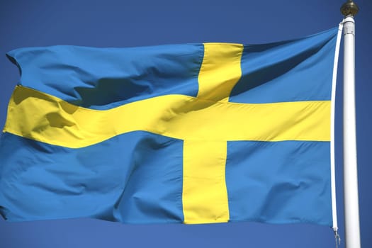 The national flag of Sweden in the colors blue and yellow waves in the wind on a flagpole. The krone is the currency of Sweden.
