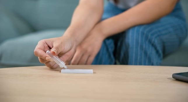 Close up woman hands using rapid antigen test kit for selftest, female four drops of liquid to perform fast coronavirus ATK self test at home in living room on sofa after lockdown and Home Isolation
