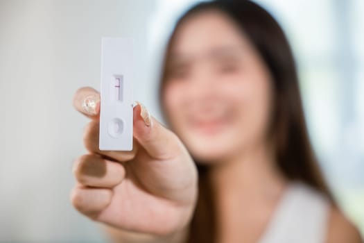 Close up woman showing rapid antigen test kit for selftest with Negative result during swab COVID-19 testing, female holding perform fast coronavirus ATK self test at home in living room, nasal