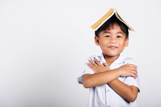 Asian adorable toddler smiling happy wearing student thai uniform red pants stand holding book over head like roof in studio shot isolated on white background, Portrait little children boy preschool