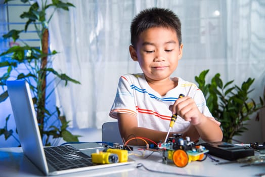 Asian kid boy assembling the Arduino robot car homework project at home, Little child tighten the nut with a screwdriver to assemble car toy, creating electronic AI technology workshop school lesson
