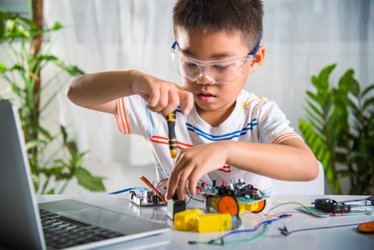 Asian kid boy assembling the Arduino robot car homework project at home, Little child tighten the nut with a screwdriver to assemble car toy, creating electronic AI technology workshop school lesson