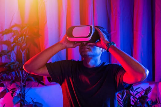 Asian handsome man wear VR helmet excited emotional at home purple and blue background, experiencing virtual reality goggles experiencing reality excited emotional, metaverse and cyberspace