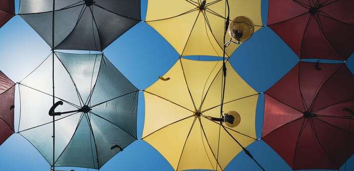 front view closeup detail of colorful umbrellas and Edison light bulbs hanging out above a city street against a blue sky