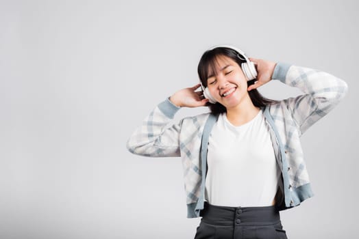 Woman excited smiling listening to music radio in bluetooth headphones and holding phone studio shot isolated white background, happy Asian young female listen modern technology mobile phone