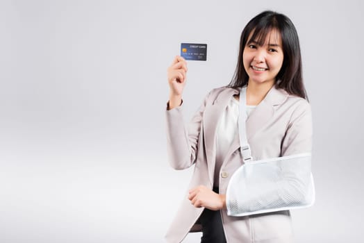 Woman confident smile broken arm after accident and wear arm splint for treatment she emergency pay medical bills by credit card, Happy Asian female sling support hand isolated on white background