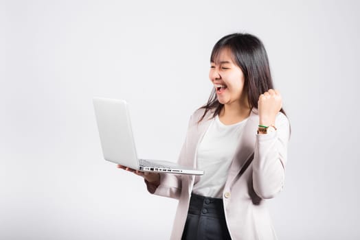 Woman smiling confident holding using laptop computer and excited celebrating success, Portrait excited happy Asian young female person say yes to win studio shot isolated on white background