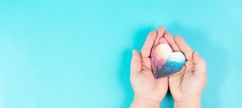 Woman is holding a colorful heart in her hand, love and charity symbol, hope concept, blue background with copy space