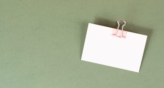 Blank white paper with a paperclip on a green colored background, copy space for text, reminder or message in the office, communication concept