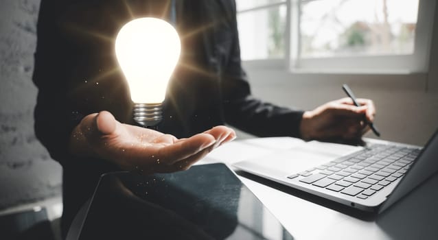 Creative iDea. Business man working with laptop computer holding light bulb on hand he is accounting and creative, businessman show lightbulb bright innovation and inspiration in energy business