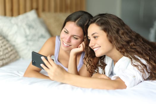 Two happy women and friends smart phone on a hotel bed