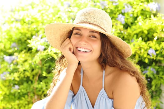 Happy woman with pamela hat smiling at camera in a green garden