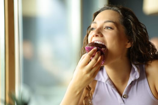 Happy woman eating chocolate cupcake in a restaurant
