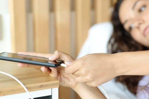 Close up of a woman connecting usb charger on smart phone in a bedroom