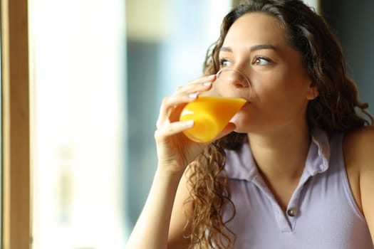 Happy woman drinking orange juice looking through window