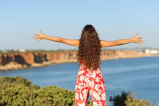 Back view portrait of a woman in red outstretching arms on the beach cliff
