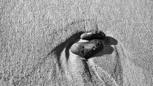 heart-shaped stone in the sand of the beach on the Baltic Seaa black and white. Romantic symbol for people in love. Small sign as still life.