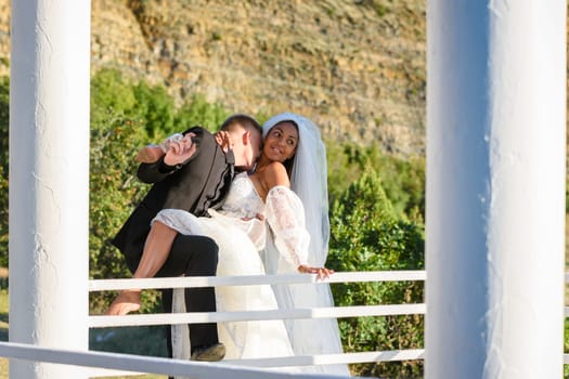 Young beautiful interracial newlyweds hugging in the gazebo, the guy kisses the neck of the girl