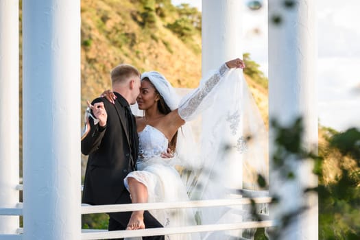 Young beautiful interracial newlyweds hugging in the gazebo