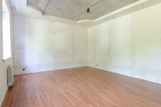 Interior of an empty room during renovation with plastered walls and laminate flooring